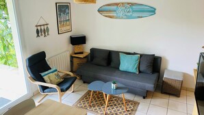 Ein modernes Wohnzimmer mit einem grauen Sofa, einem Holzstuhl, einem kleinen Tisch und einem dekorativen Surfbrett an der Wand.