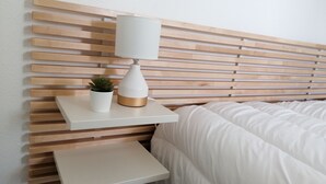 Ein Bett mit weißer Bettwäsche, ein Nachttisch mit einer Lampe und ein kleiner Blumentopf.