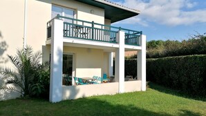 Ein zweigeschossiges Haus mit einem Balkon, einer überdachten Terrasse mit Stühlen und einem gepflegten Rasen.