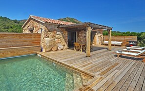 Une terrasse en bois avec une piscine à eau claire, des murs en pierre et une pergola en bois.