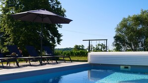 Une piscine d’un bleu éclatant, avec des chaises longues et un parasol, le tout entouré d’arbres.