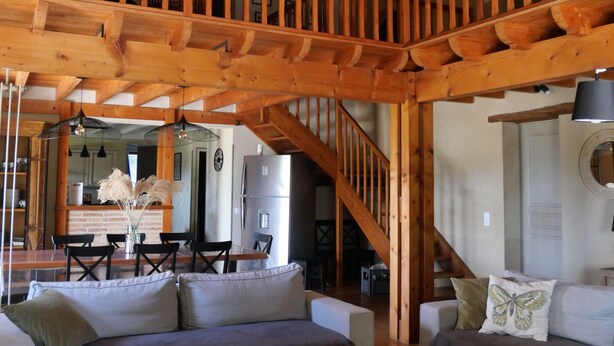 Un vaste espace de vie doté d’un haut plafond en bois et d’un escalier en bois. On y trouve deux canapés et une table basse agrémentée d’objets décoratifs.