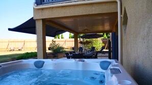 Un bain à remous avec un espace patio, du mobilier d’extérieur et une clôture en bois en arrière-plan.
