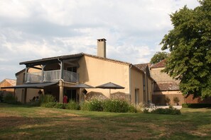 Ein zweigeschossiges Haus mit Balkon, Schornstein und einem Garten mit Blumen und einem Baum.