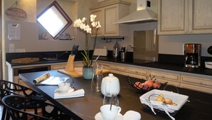 Une cuisine moderne avec des meubles blancs, un grand îlot central où l’on peut prendre le petit-déjeuner, et des luminaires suspendus.