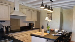 Une cuisine moderne avec des armoires en bois, un comptoir noir et un îlot central doté d’une planche à découper. On y trouve trois lampes suspendues, une machine à café et une orchidée en pot sur l’îlot.