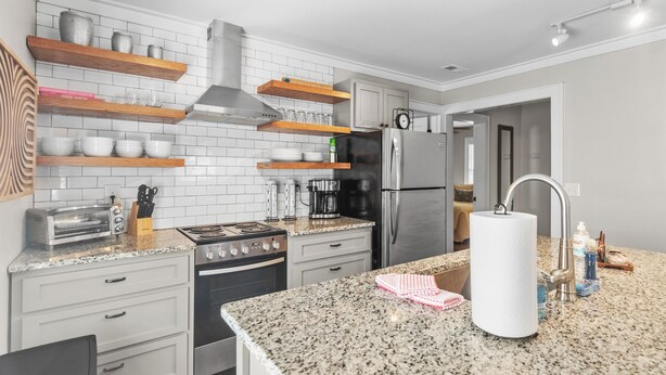 Une cuisine moderne dotée de plans de travail en granit, d’appareils électroménagers en acier inoxydable et d’étagères en bois.