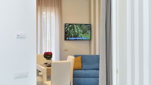 Een moderne woonkamer met een eethoek, een wandtelevisie en een gedeeltelijk dichtgemaakte grijze gordijn.