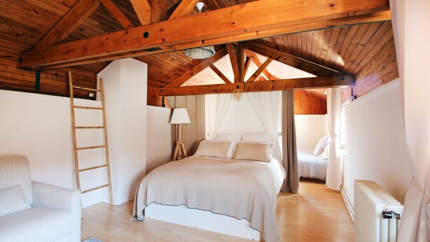Une chambre avec un plafond en bois, un lit, une chaise, une échelle et un radiateur.