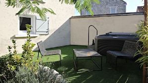Un petit patio extérieur avec du gazon synthétique, deux chaises à motifs, une petite table et un jacuzzi.
