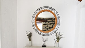 Une console blanche, surmontée d’un miroir rond, et agrémentée de deux petits vases contenant des plantes séchées.