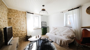 Une pièce confortable avec un mur en pierre, un lit, une télévision, une petite table et une chaise.