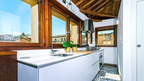 A kitchen with a large island, wooden beams, and a view of buildings through large windows. - Genteel Home Zacatin Penthouse 401 (Granada)