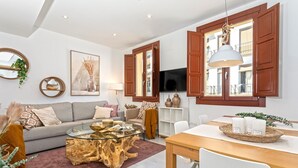 Una sala de estar moderna con una mesa de centro de vidrio, una mesa de comedor de madera y un televisor montado en la pared.
