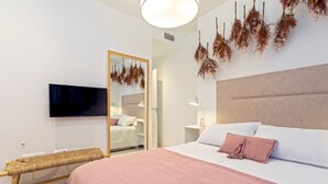 Un dormitorio moderno con una cama, un televisor, un espejo y flores secas colgadas.
