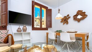 Una sala de estar moderna con un televisor de pantalla plana grande, muebles de madera y un comedor con sillas blancas.