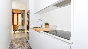 Eine moderne Küche mit weißen Schränken, einer schwarzen Induktionskochplatte, einem Edelstahl-Spülbecken und einem kleinen Topf mit Pflanze.