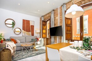 A modern living room with a sofa, TV, dining table, and a brick wall.