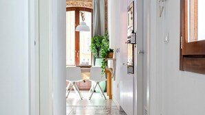A narrow hallway with a patterned floor leading to a dining area with chairs and a table, a potted plant, and a refrigerator.