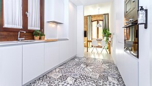 A modern kitchen with white cabinets, a patterned floor, and a wooden door with curtains.