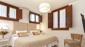 A bedroom with a large bed, wooden shutters, a bedside table with a lamp, and a chair. - Genteel Home Zacatin 103 (Granada)
