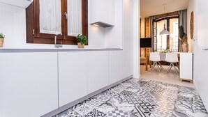 A modern kitchen with white cabinets, a patterned tile floor, and a window with curtains.