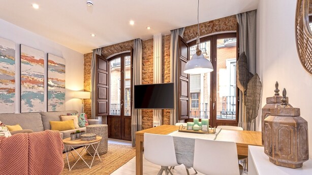 A modern living room with a sofa, a coffee table, a TV, and a dining area with chairs and a table.