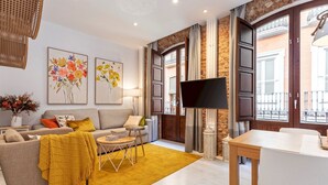Una sala de estar moderna con sofá, mesa de centro y televisor, destacando una pared de piedra y grandes ventanales.