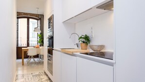 Una cocina moderna con armarios blancos, encimera de madera y horno empotrado. Se ve un área de comedor con una mesa y sillas al fondo.