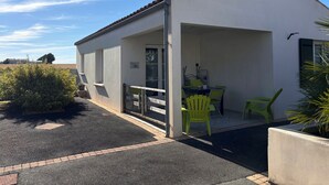 Un edifici blanc amb terrassa coberta, taula i cadires, i una petita zona de jardí.