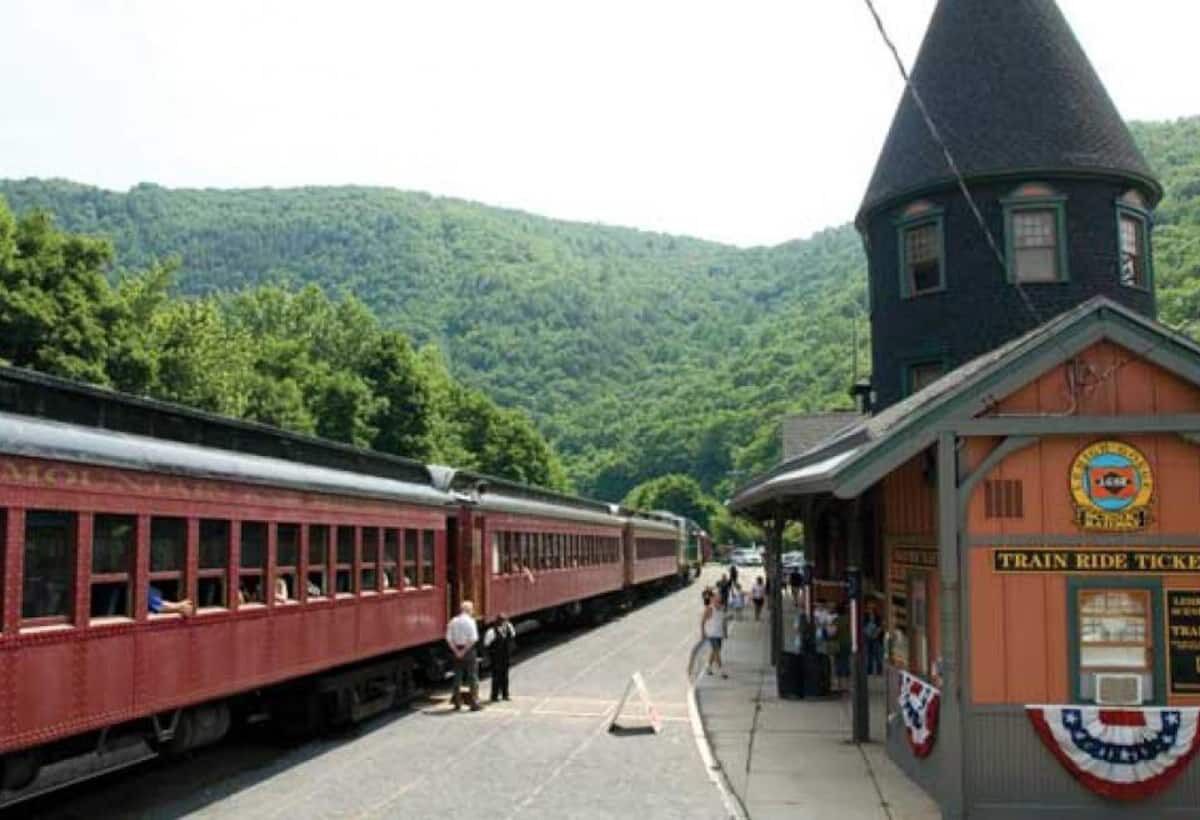 Una stazione ferroviaria con un treno rosso d'epoca, un edificio a forma di cono e un binario affollato di persone.