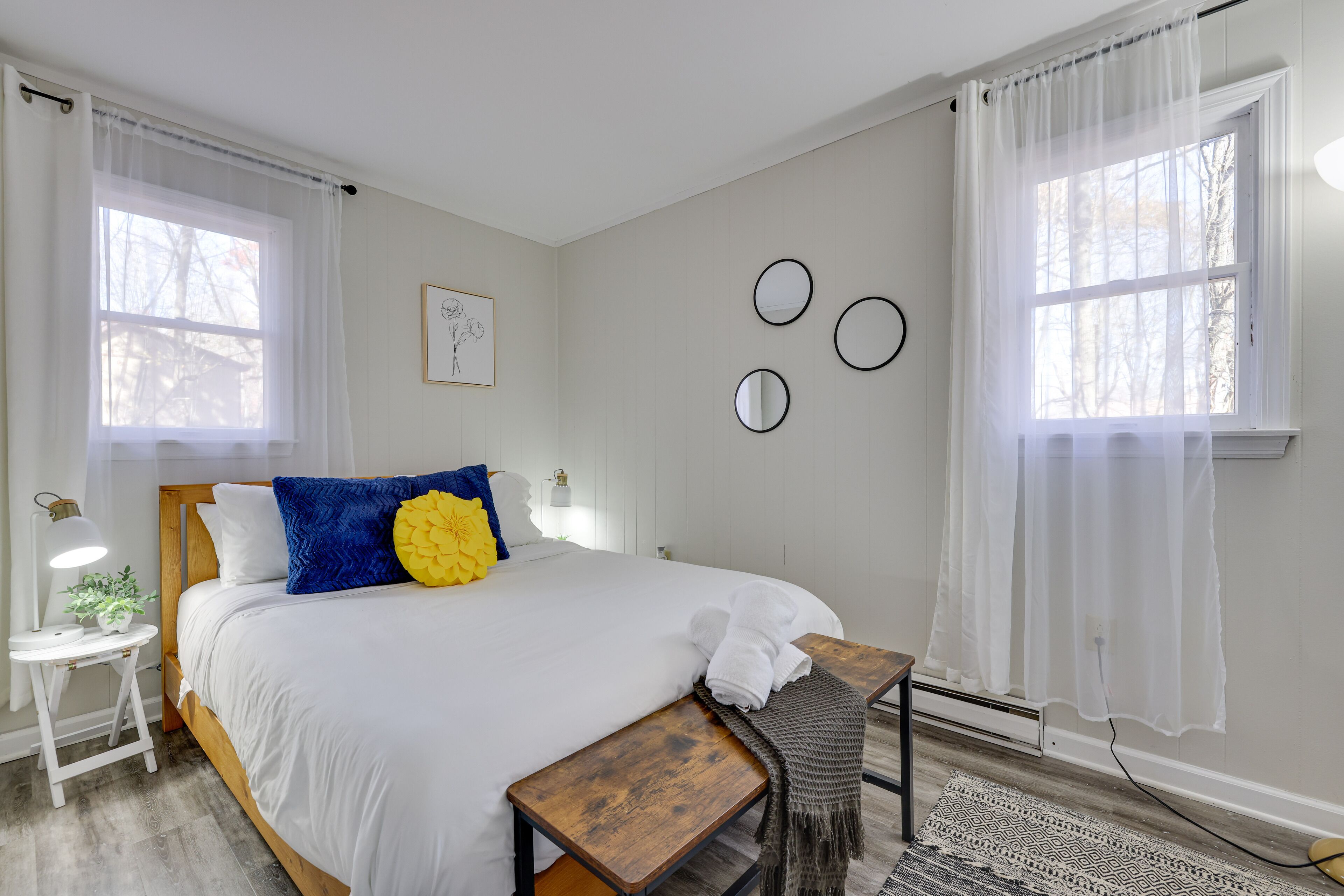 Quarto com cama, mesa de cabeceira, abajur e uma parede com três espelhos redondos.