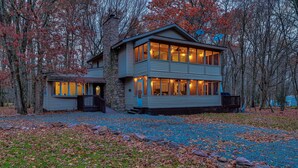 A two-story house with a stone chimney, large windows, and a covered porch.