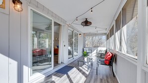 A covered porch with glass doors leading to a room, a ceiling fan, and a red bag on a chair.