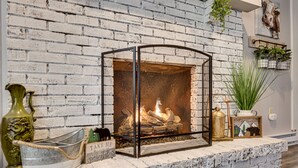 A fireplace with a metal frame, a brick wall, and a shelf with decorative items.