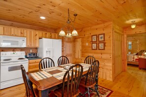 A wooden cabin interior with a dining table, chairs, a kitchen with a stove and microwave, and a ceiling light fixture. - Long Mtn. Views - Covered Porch - Rockers - Fire Pit - Gated - Clean - 5 Stars! (Waynesville)
