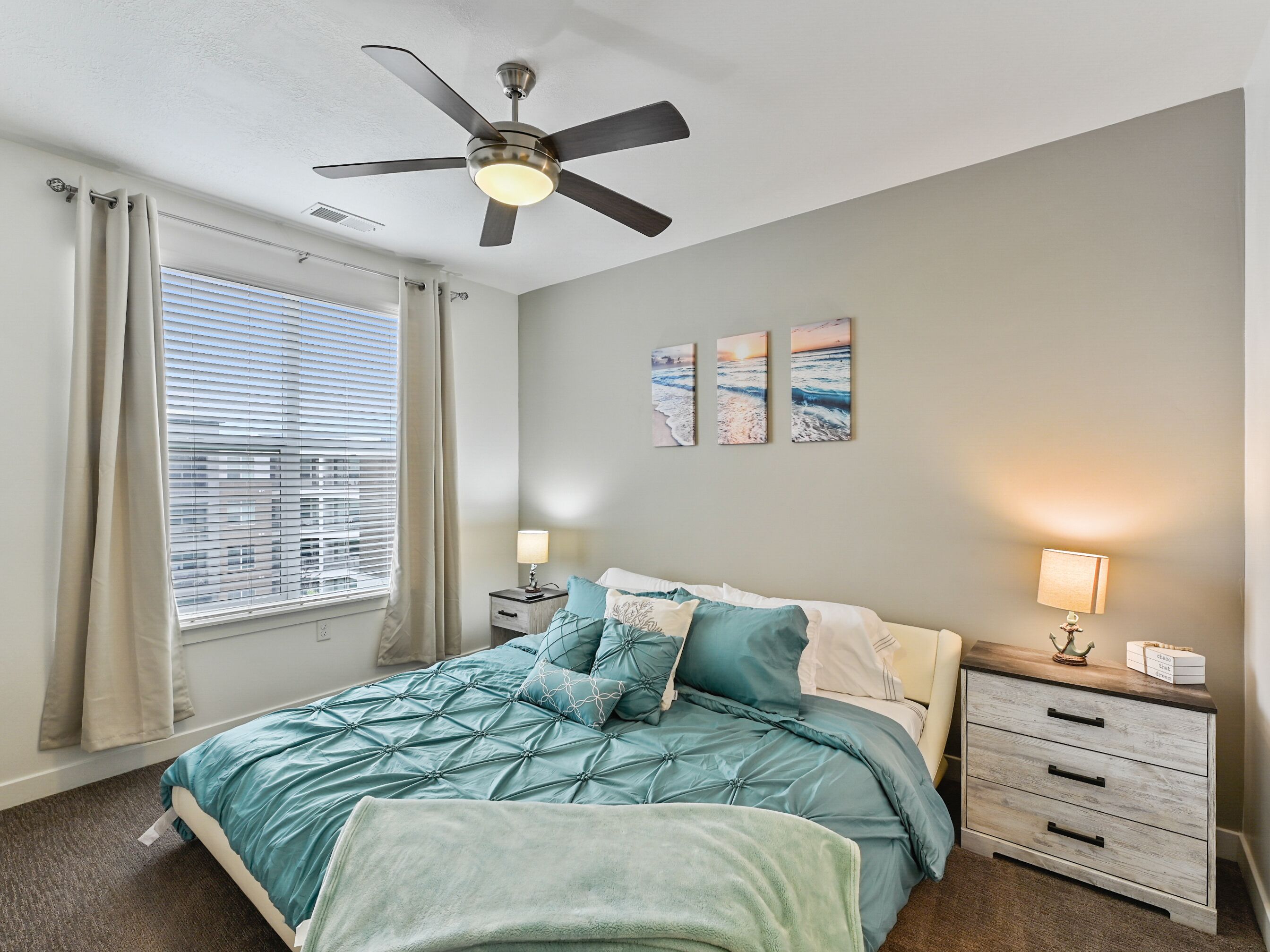Une chambre à coucher comprenant un lit, deux tables de chevet, un ventilateur de plafond et une fenêtre avec des rideaux.
