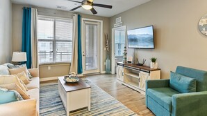 A living room with a sofa, a coffee table, a TV, and a ceiling fan. - Family Friendly Beach Theme with Hot Tub! (Draper)
