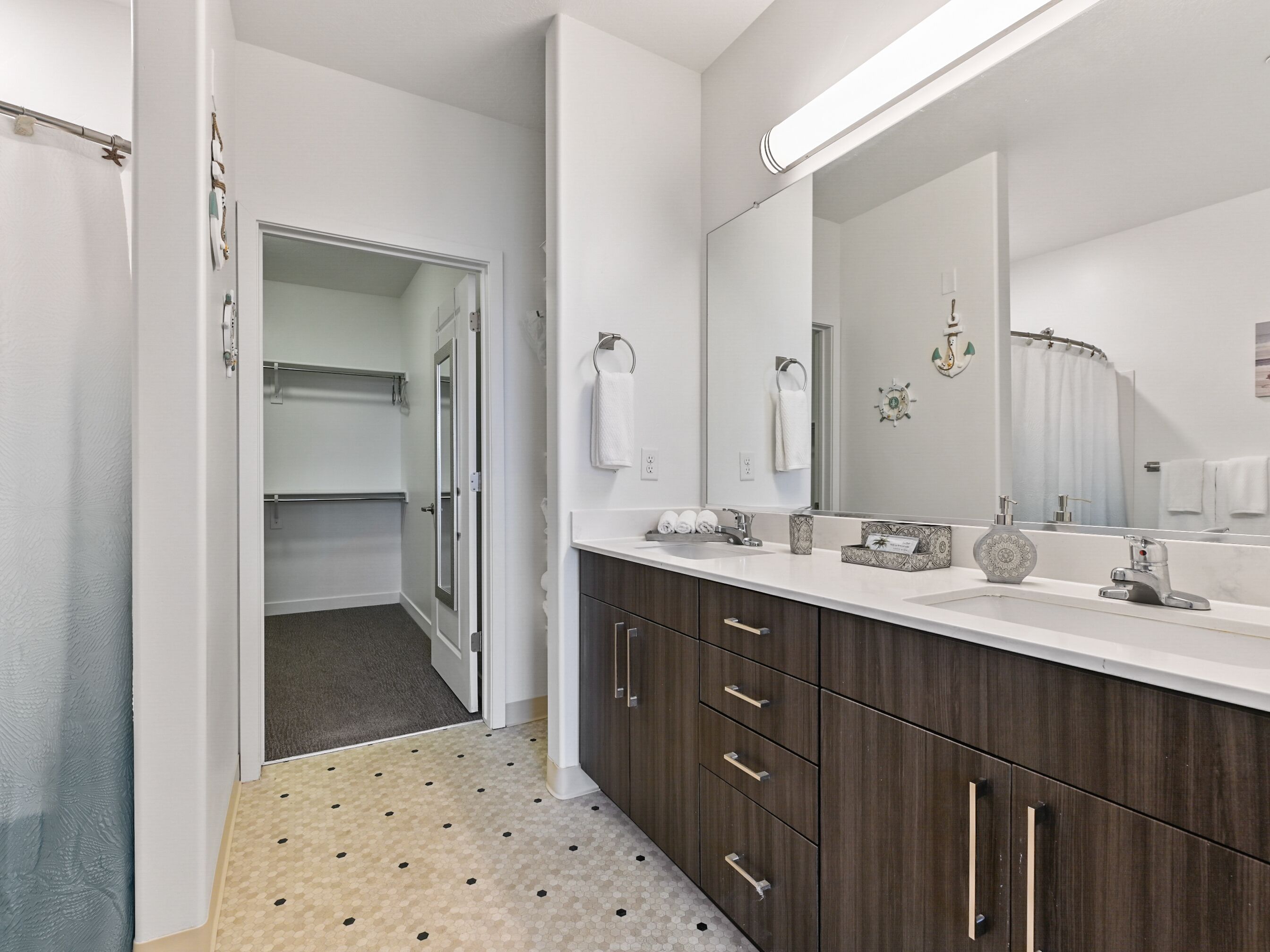 Un baño moderno con un espejo grande, armarios de madera oscura y una encimera blanca.