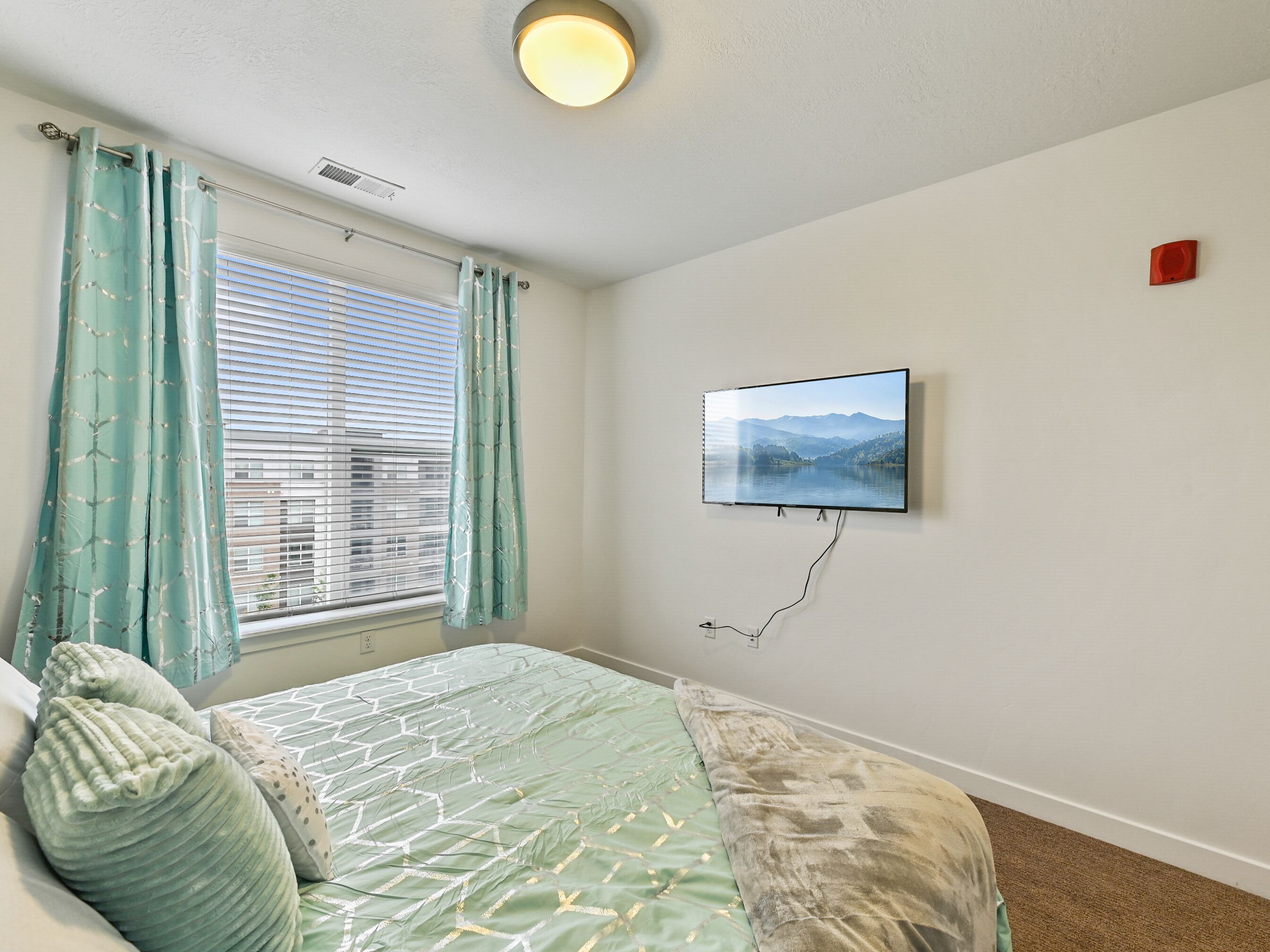 Ein Schlafzimmer mit Bett, einem fensterbelaubten Fenster, einem an der Wand montierten Fernseher und einem roten Notfalllicht.