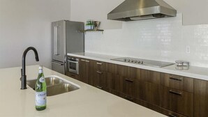 A modern kitchen with a stainless steel refrigerator, a built-in oven, a stainless steel range hood, and a white countertop. - Family Friendly Beach Theme with Hot Tub! (Draper)