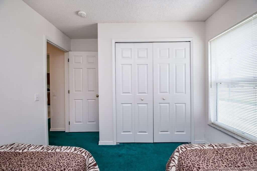 A room with two leopard-print beds, a teal carpet, white walls, and a white closet with two doors.