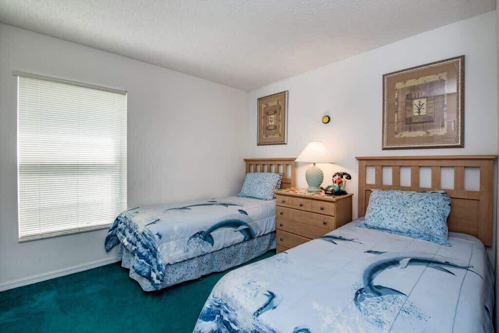 A bedroom with two beds, a nightstand, a lamp, and framed pictures on the wall.