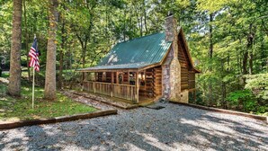 Ein rustikales Blockhaus mit Steinofen, umgeben von Bäumen und einem Schotterweg.