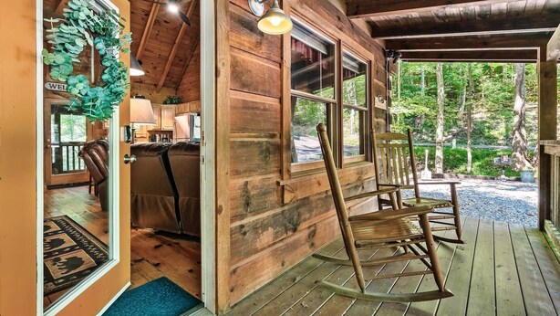 Eine Holzhütte mit Veranda, einem Willkommen-Kranz und Blick auf den Wald.