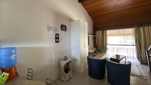 Une pièce avec un plafond en bois, une armoire blanche, un canapé, une table à manger avec des chaises et un distributeur d’eau bleu.