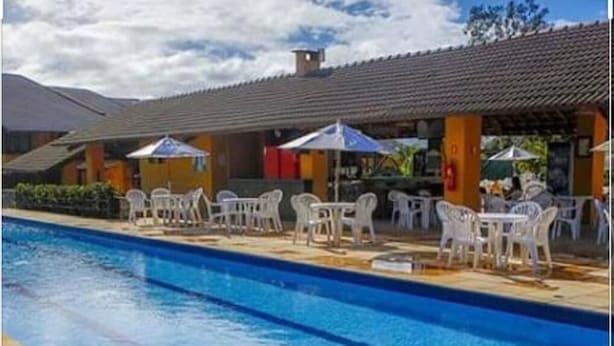 Une piscine entourée de chaises blanches et de parasols, elle-même bordée d’une zone couverte dotée d’un toit en tuiles.