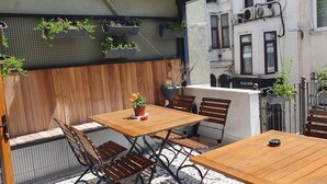 A wooden table and chairs set in an outdoor patio area with hanging planters and a tiled wall. - Taksim suite (Istanbul)