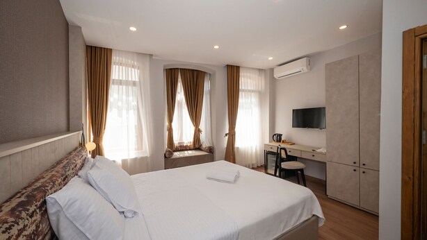 A hotel room with a large bed, a desk with a chair, a television, and an air conditioning unit. - Taksim suite (Istanbul)