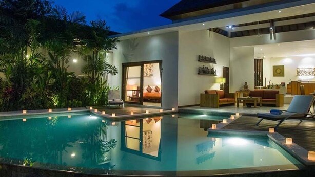 A modern hotel with a large indoor swimming pool, a well-lit living area, and a tropical garden.